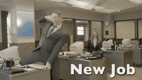 a man in a suit and tie is sitting on a desk in an office with the words `` new job '' above him .