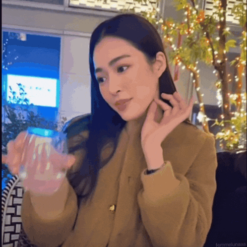 a woman in a brown coat holds a glass of water in her hand