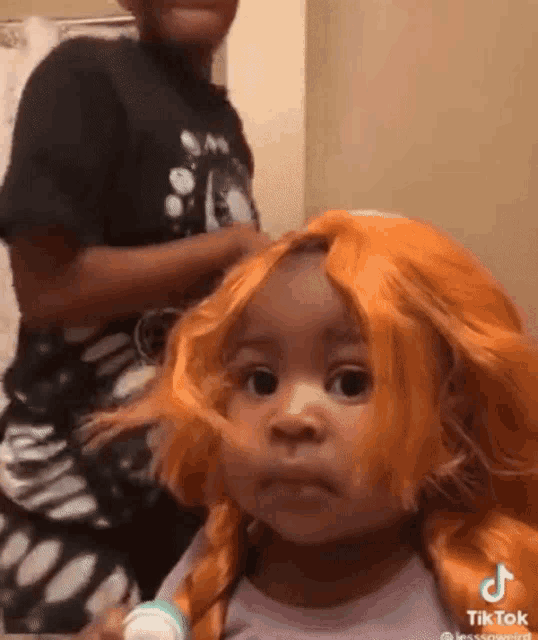 a little girl wearing an orange wig is being brushed by a man .