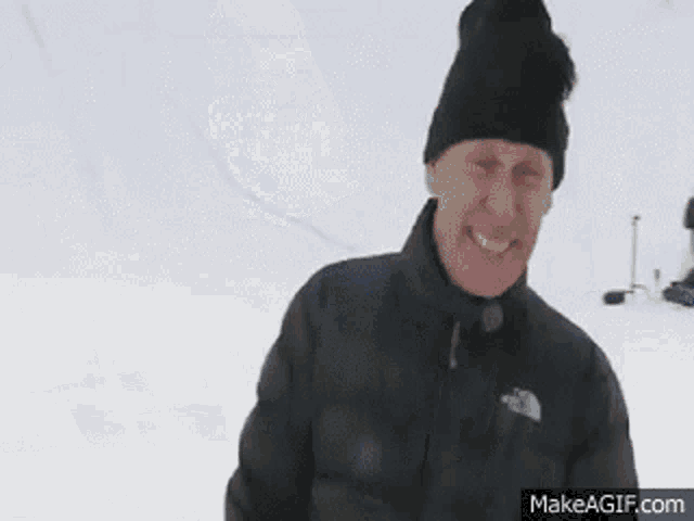 a man is crawling in the snow while wearing a black jacket and hat .