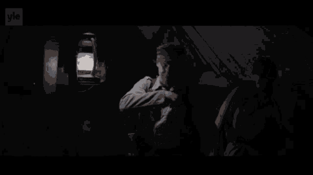 two men are standing in a dark room with a lantern hanging from the ceiling and the word yle on the bottom right