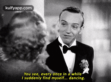 a black and white photo of a man in a tuxedo talking to another man .