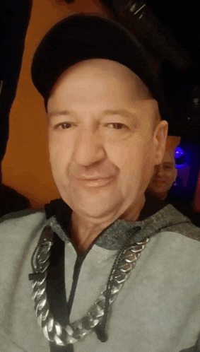 a bald man wearing a black hat and a chain around his neck