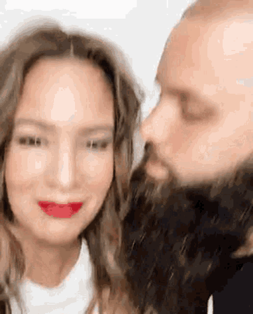 a man with a beard and a woman with red lipstick are kissing .