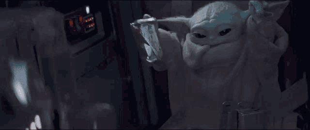 a baby yoda is sitting in a chair and holding a bag of food in his hand .