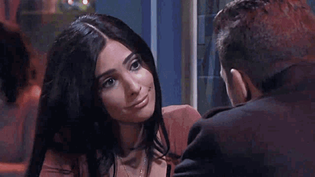 a man and a woman are sitting at a table looking at each other and smiling .