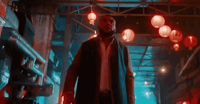 a man with a beard is standing in a dark alleyway surrounded by lanterns .