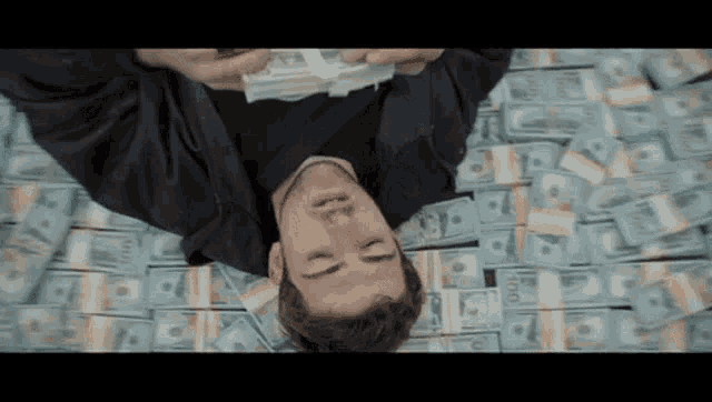 a man is laying on top of a pile of money holding a stack of money .