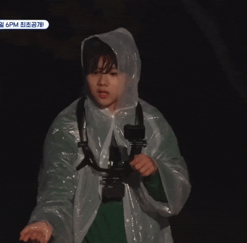 a person wearing a clear plastic raincoat holds a camera in their hand