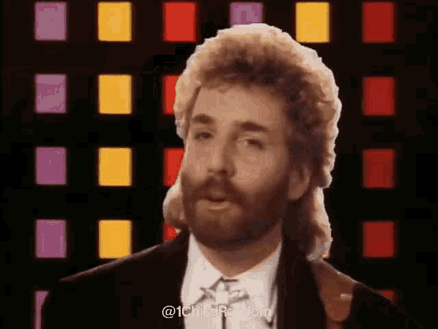 a man with a mullet and a beard is standing in front of a wall of squares .