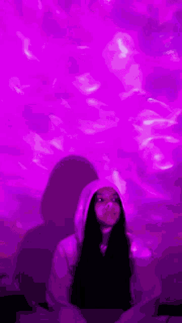 a woman in a hoodie is standing in front of a purple light projection .