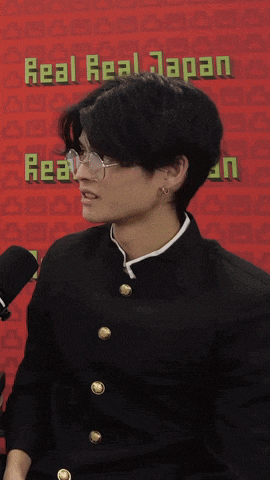 a man wearing glasses is standing in front of a red background that says real real japan