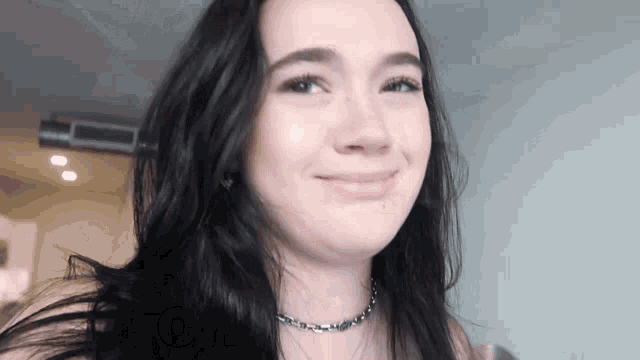 a woman with long black hair is smiling and wearing a necklace