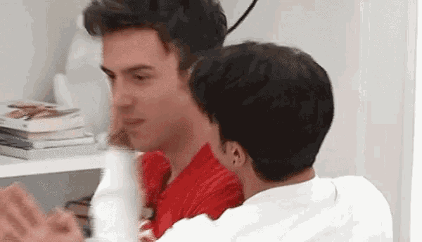 two men are sitting next to each other in a room and one of them is wearing a red shirt .