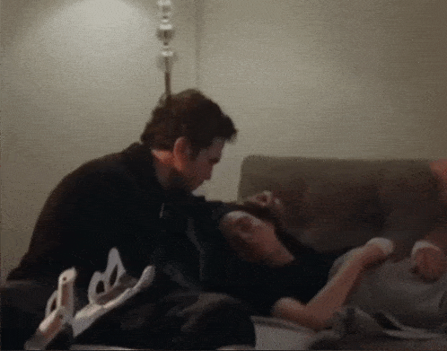 a man laying on a couch next to a woman with a broken arm