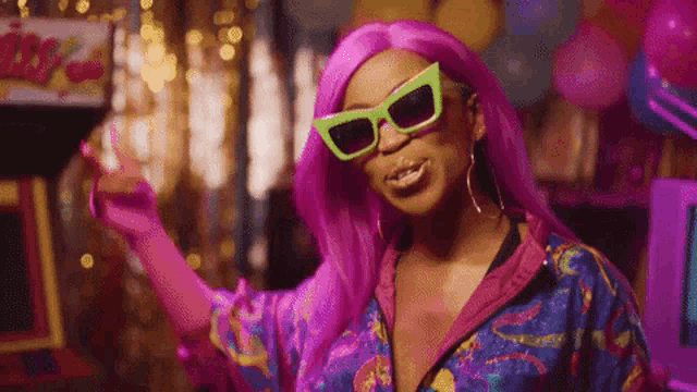 a woman with pink hair and green sunglasses is wearing a colorful outfit and dancing .