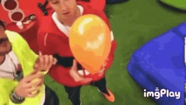 a man is holding an orange balloon in his hand while another man blows it up .