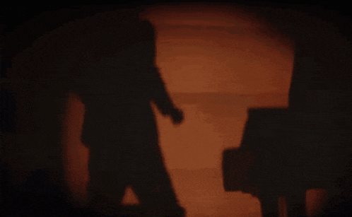 a shadow of a person walking in a dark room with a piano in the background