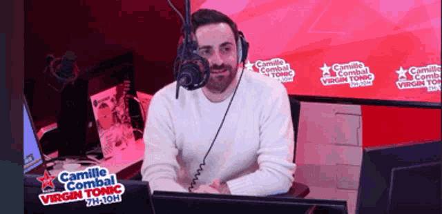 a man sitting in front of a microphone with camille combal virgin tonic written on the wall behind him