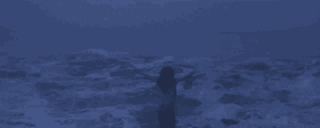 a woman in a white shirt is standing in the ocean