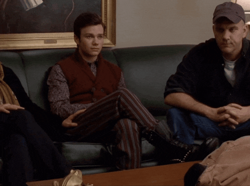 a man in a red vest sits on a green couch with other people