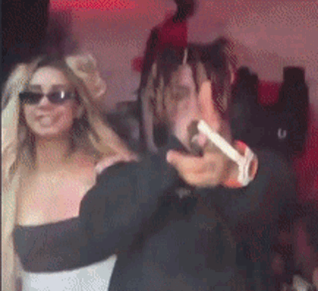 a man and a woman are standing next to each other in a room . the woman is wearing sunglasses .