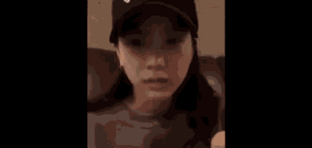 a woman wearing a hat and a t-shirt is sitting on a couch and talking on a cell phone .