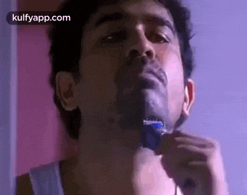 a man is shaving his beard with a razor in front of a mirror .