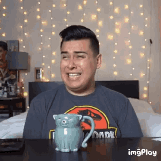 a man wearing a jurassic park shirt is crying while sitting at a desk