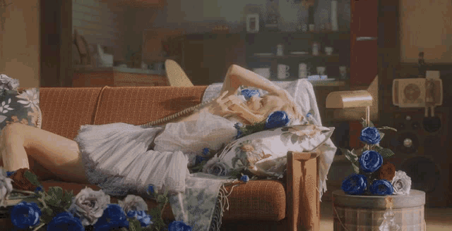 a woman sits on a couch surrounded by flowers and a teddy bear