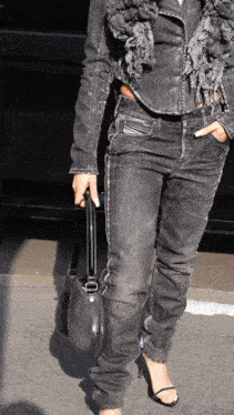 a woman wearing a denim jacket and jeans holds a black bag