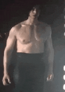 a man without a shirt is standing in the dark in front of a light .