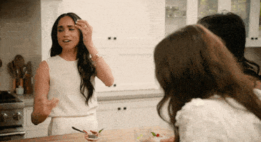 a woman in a white dress is standing in a kitchen with two other women