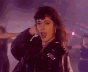 a woman in a black leather jacket is dancing in a dark room with purple lights .