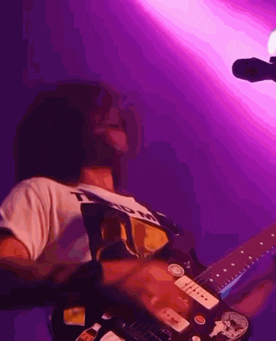 a man is playing a guitar in front of a microphone in a purple room .