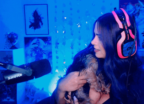 a woman wearing headphones and a shure microphone holds a small dog