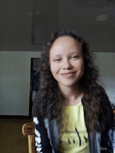 a girl with curly hair is smiling and wearing a yellow shirt that says ' smiley face '