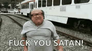 a man is standing on train tracks next to a train and saying `` fuck you satan ! ''