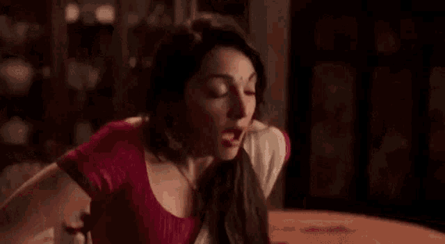 a woman is sitting at a table with her eyes closed . she is wearing a red blouse and a white sari .