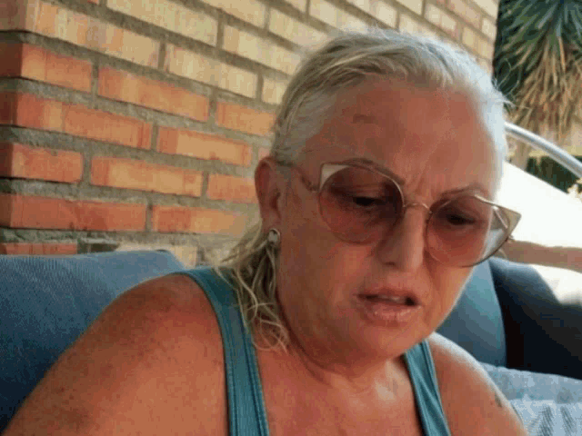 a woman wearing sunglasses sits on a couch with a brick wall in the background