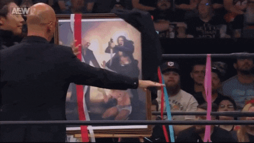 a man is holding a framed picture of a woman in a wrestling ring with a aew logo in the corner