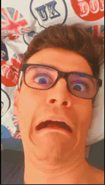 a man wearing glasses is making a funny face in front of a bedspread with uk on it