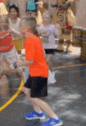 a blurry picture of a boy in an orange shirt and blue shoes playing with a hula hoop .
