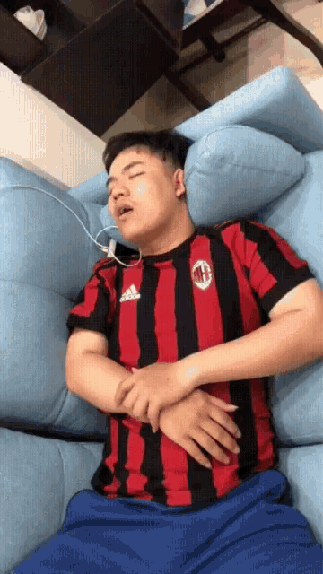a man wearing a red and black adidas shirt is sleeping on a blue couch