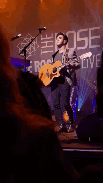 a man playing a guitar in front of a sign that says the rose