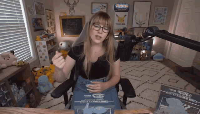 a woman sitting in a chair looking at a box that says elite trainer box