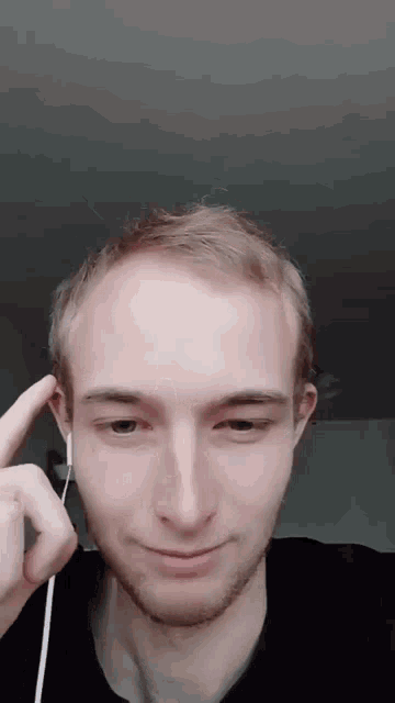 a young man wearing ear buds looks at the camera and smiles