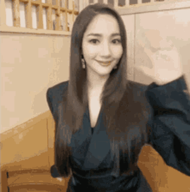 a woman with long hair is wearing a black jacket and waving at the camera .