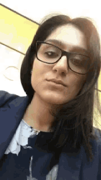 a woman wearing glasses and a blue jacket is making a face .