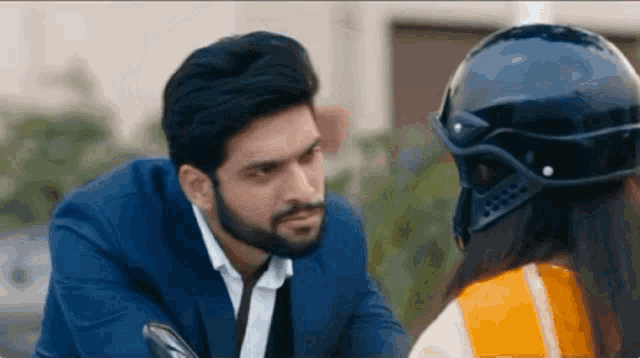 a man in a suit and a woman in a helmet are sitting on a motorcycle and looking at each other .
